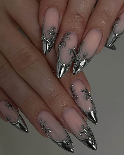 Nude nails laid flat with silver ornate French tips that swirl down towards the nail base.