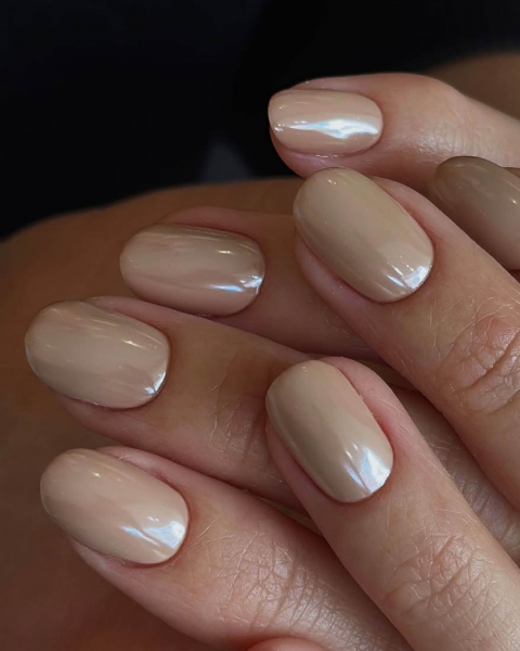 Nudecolored shimmery nails on hands clasped together.