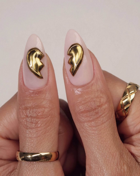 Thumbs pointed out each nude nail featuring one side of a split gold broken heart.