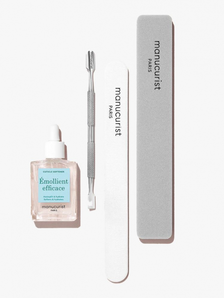 A small bottle of cuticle softener, along with a cuticle pusher and nail files lying flat. 